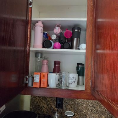 Sale Photo Thumbnail #74: Assorted travel mugs, water bottles, and coffee cups stored inside a wooden kitchen cabinet.