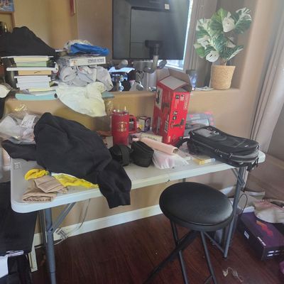 Sale Photo Thumbnail #82: White plastic folding table cluttered with various household items, including a black folding stool, clothing, a red Craftsman tool box, and a red travel mug.