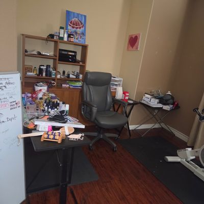 Sale Photo Thumbnail #14: Home office setup featuring a grey faux-leather rolling desk chair, a wooden bookcase, a whiteboard, and various small tables with office supplies.