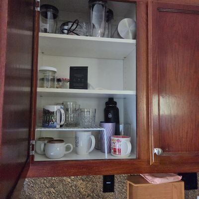 Sale Photo Thumbnail #75: Assorted kitchenware, including mugs, tumblers, and blender cups, organized inside a wooden upper cabinet.