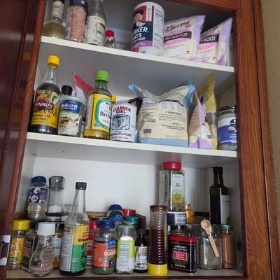 Sale Photo Thumbnail #73: Assorted pantry items, spices, and baking ingredients organized on three shelves inside a wooden kitchen cabinet.
