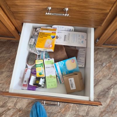 Sale Photo Thumbnail #50: An assortment of personal care and first aid items, including adhesive pads, earwax removal drops, and a hairbrush, stored inside a wooden vanity drawer.