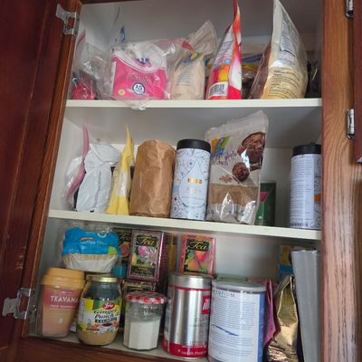 Sale Photo Thumbnail #71: Assorted pantry items, including teas, coffee, and baking ingredients, organized on three shelves inside a wooden kitchen cabinet.
