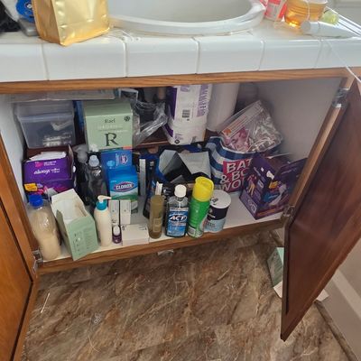 Sale Photo Thumbnail #52: Assorted household cleaning supplies, personal care products, and toiletries stored under a bathroom sink vanity.
