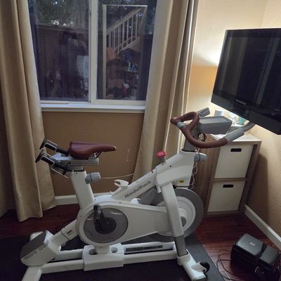 Sale Photo Thumbnail #6: NordicTrack Commercial S22i Studio Cycle stationary exercise bike, featuring a white frame, brown leather-style seat and handlebars, and a large rotating touchscreen display.
