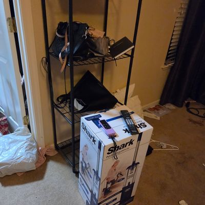 Sale Photo Thumbnail #28: Shark Navigator upright vacuum cleaner in its original box, shown alongside a black metal wire shelving unit holding various handbags and accessories.