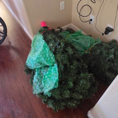 Sale Photo Thumbnail #42: Disassembled artificial Christmas tree sections wrapped in green bubble wrap, sitting on a hardwood floor.