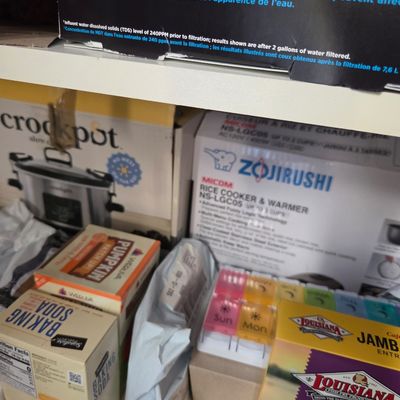 Sale Photo Thumbnail #79: Assorted pantry items and small kitchen appliances in boxes, including a Zojirushi rice cooker, a Crockpot, and various packaged food items.