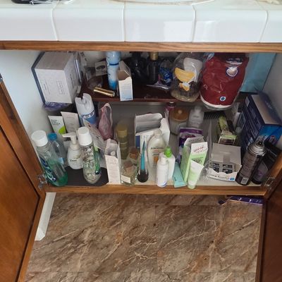 Sale Photo Thumbnail #59: Assorted personal care products, toiletries, and cosmetics stored inside a wooden bathroom vanity cabinet.