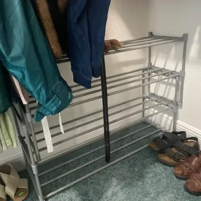 Four-tier grey plastic and metal shoe rack with assorted footwear including sandals and leather loafers.