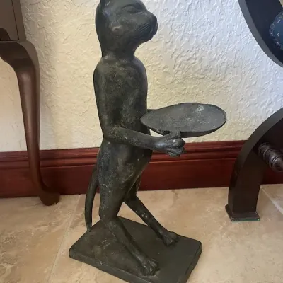 Cast dark metal cat butler statue holding a tray, set on a rectangular base with an aged dark patina.