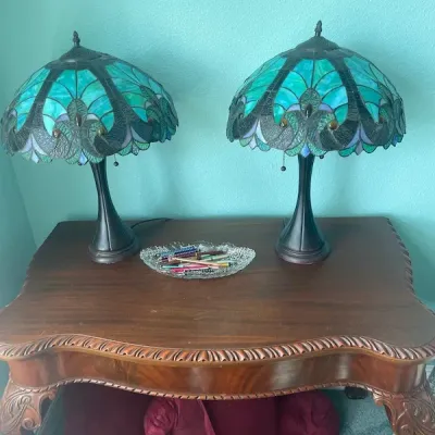 Pair of Tiffany-style leaded stained glass table lamps with peacock feather motif shades in shades of teal and blue, resting on a carved...