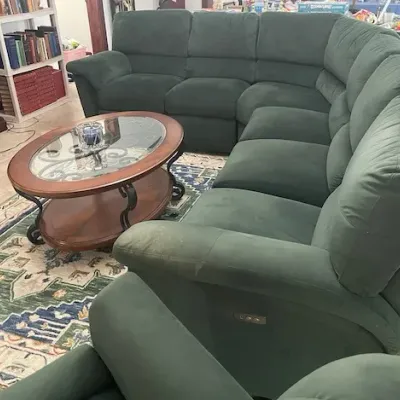 Large dark green microfiber sectional sofa paired with an oval wood and glass coffee table featuring scrollwork metal legs.