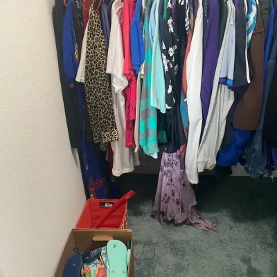 Closet packed with various women's clothing on hangers, with boxes of sandals and storage bins on the floor below.