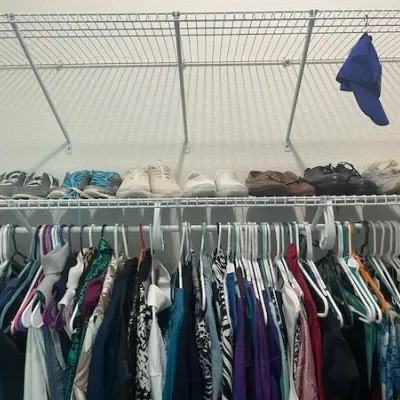 Closet filled with women's hanging clothing and assorted shoes, including sneakers and loafers, displayed on wire shelving.