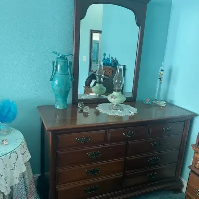 Traditional dark wood dresser with matching arched mirror, featuring multiple drawers with metal pulls. Styled with decorative glassware,...