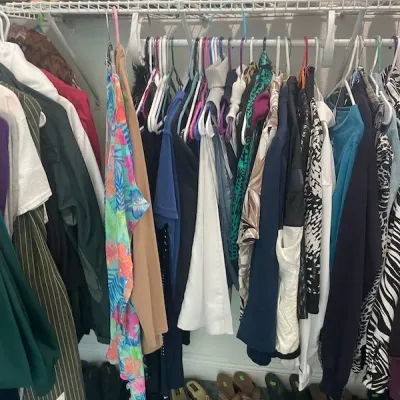 Closet filled with women's clothing on hangers alongside various pairs of shoes arranged on top wire shelving and on the floor.