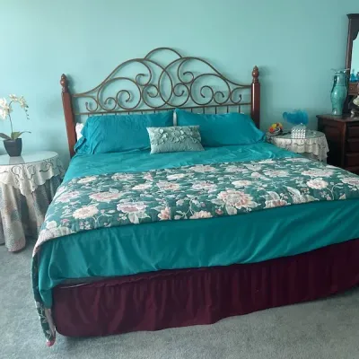 King-size bed featuring an ornate metal scrollwork headboard with wooden corner posts, styled with teal linens and a floral runner.