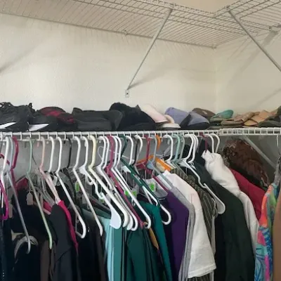 Walk-in closet loaded with hanging women's clothing and shoes lined up on an upper wire shelf.
