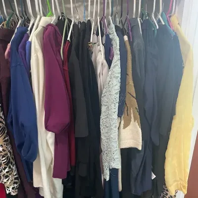 Closet packed with various women's clothing items hanging on plastic and wire hangers, including sweaters, blouses, jackets, and...