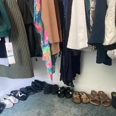 Closet filled with women's hanging clothing and an array of shoes lined up along the carpeted floor below.
