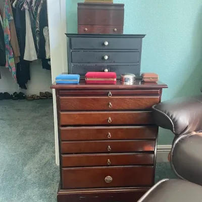 Traditional cherry-finished jewelry chest featuring multiple drawers, topped with additional desktop jewelry boxes and trinket cases.