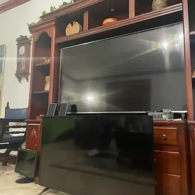 Large wooden entertainment center wall unit featuring open shelving, cabinetry, and a large flat-screen television, accompanied by...
