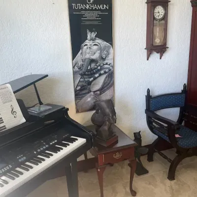 Technics digital piano alongside a framed vintage "Treasures of Tutankhamun" exhibition poster, an Egyptian bust on a wooden...