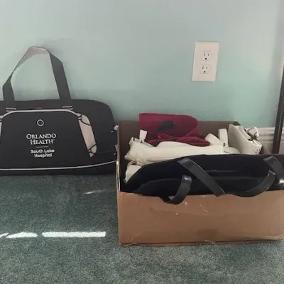 Black Orlando Health South Lake Hospital duffel bag alongside a cardboard box filled with various handbags.