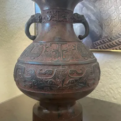 Asian-style dark metal vase featuring relief taotie mask carving and elephant head handles.