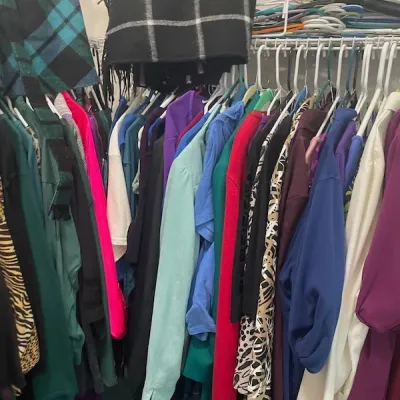 Closet packed with assorted women's clothing, scarves, and accessories hanging on a wire rack.