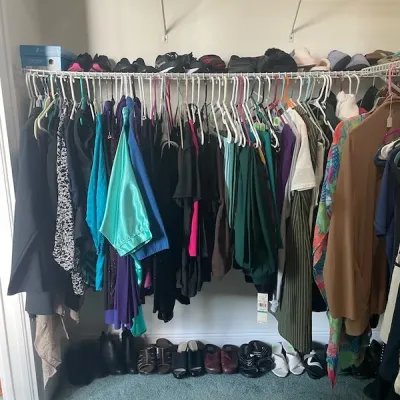 Closet filled with women's clothing on hangers, with footwear arranged on the top shelf and floor below.