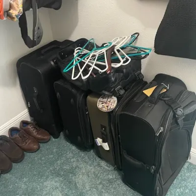 Collection of black and olive rolling luggage bags with a pile of plastic clothes hangers on top, accompanied by men's casual shoes.
