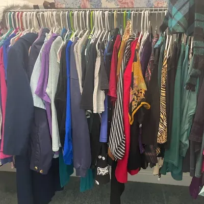 Closet rack packed with assorted women's clothing, including jackets, sweaters, tops, and patterned scarves on plastic hangers.