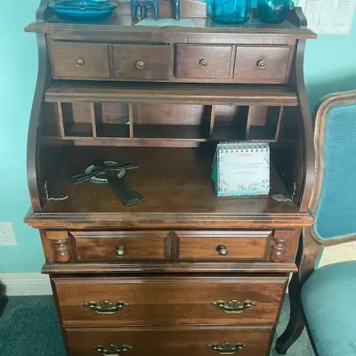 Vintage dark wood roll-top secretary desk featuring upper organizers, multiple drawers with brass hardware, and displayed decorative...