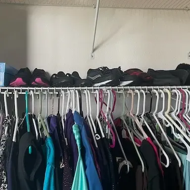 Closet rack lined with women's hanging clothing and an assortment of shoes and shoeboxes on the wire shelf above.