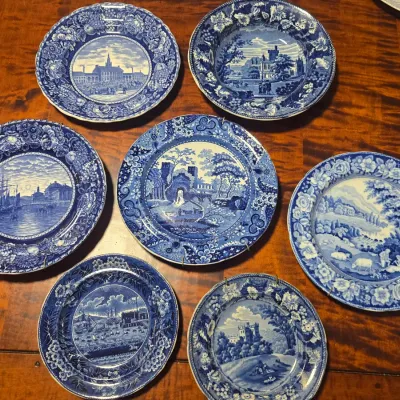 Collection of seven vintage blue and white transferware plates, featuring various historical scenes, landscapes, and floral borders.
