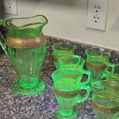 Vintage uranium glass pitcher and matching footed mugs, featuring ornate gold-encrusted bands and gold-trimmed rims.