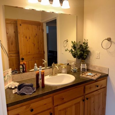 Sale Photo Thumbnail #35: Rustic pine bathroom vanity with a dark laminate countertop, white drop-in sink, and a four-light vanity fixture above a large frameless mirror.
