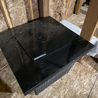 Sale Photo Thumbnail #16: Modern square outdoor fire pit table featuring a glossy black glass top with a removable center lid and a dark woven wicker-style base.
