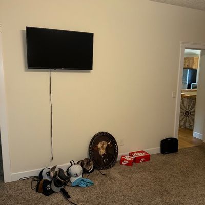Sale Photo Thumbnail #28: Wall-mounted flat-screen television, accompanied by a collection of baseball caps, a framed highland cow portrait, and Nike shoeboxes on the floor.