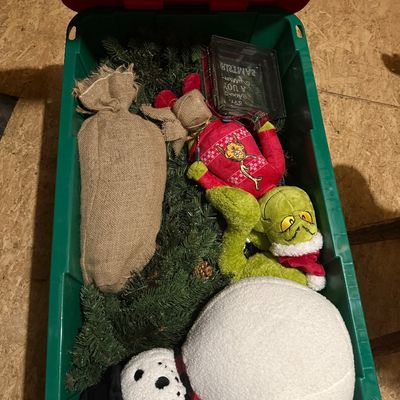 Sale Photo Thumbnail #48: Assorted Christmas decorations stored in a green plastic bin, including a plush snowman, a Grinch plush toy, a burlap sack, and artificial pine garland.