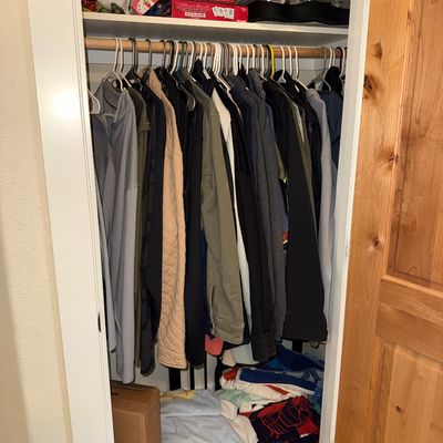 Sale Photo Thumbnail #30: Assorted men's jackets, sweaters, and activewear hanging in a closet, with board games on the top shelf and folded blankets below.