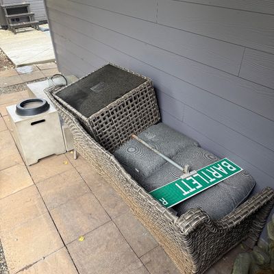 Sale Photo Thumbnail #54: Woven resin wicker outdoor chaise lounge with grey cushions, shown alongside a green metal "BARTLETT" street sign.
