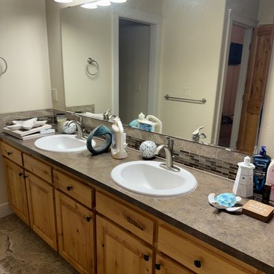 Sale Photo Thumbnail #22: Rustic pine double vanity with a dark laminate countertop, dual white undermount sinks, brushed nickel faucets, and a large frameless wall mirror.