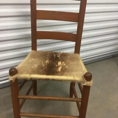 Vintage wooden ladder-back chair featuring a rustic cowhide-covered seat.