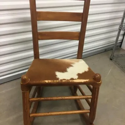 Rustic wooden ladder-back rocking chair featuring a cowhide upholstered seat.