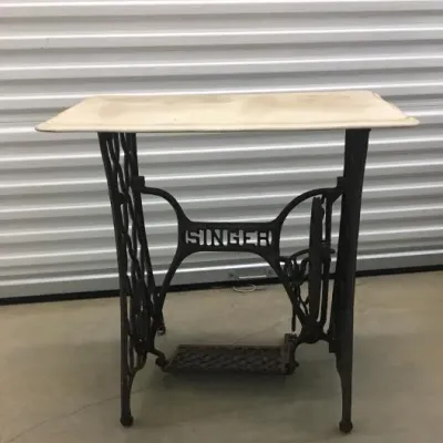 Vintage Singer sewing machine treadle base repurposed as a small table with a light-colored rectangular top.