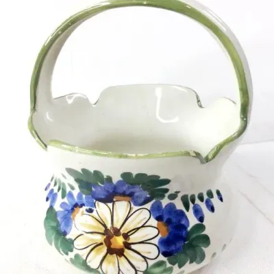Vintage hand-painted ceramic basket planter featuring a scalloped rim, green handle, and vibrant blue and yellow floral motifs.