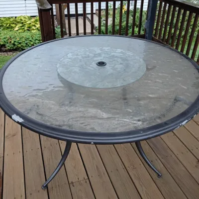 Sale Photo Thumbnail #66: Round outdoor patio table featuring a tempered water-glass top with a central umbrella hole and a dark metal frame.